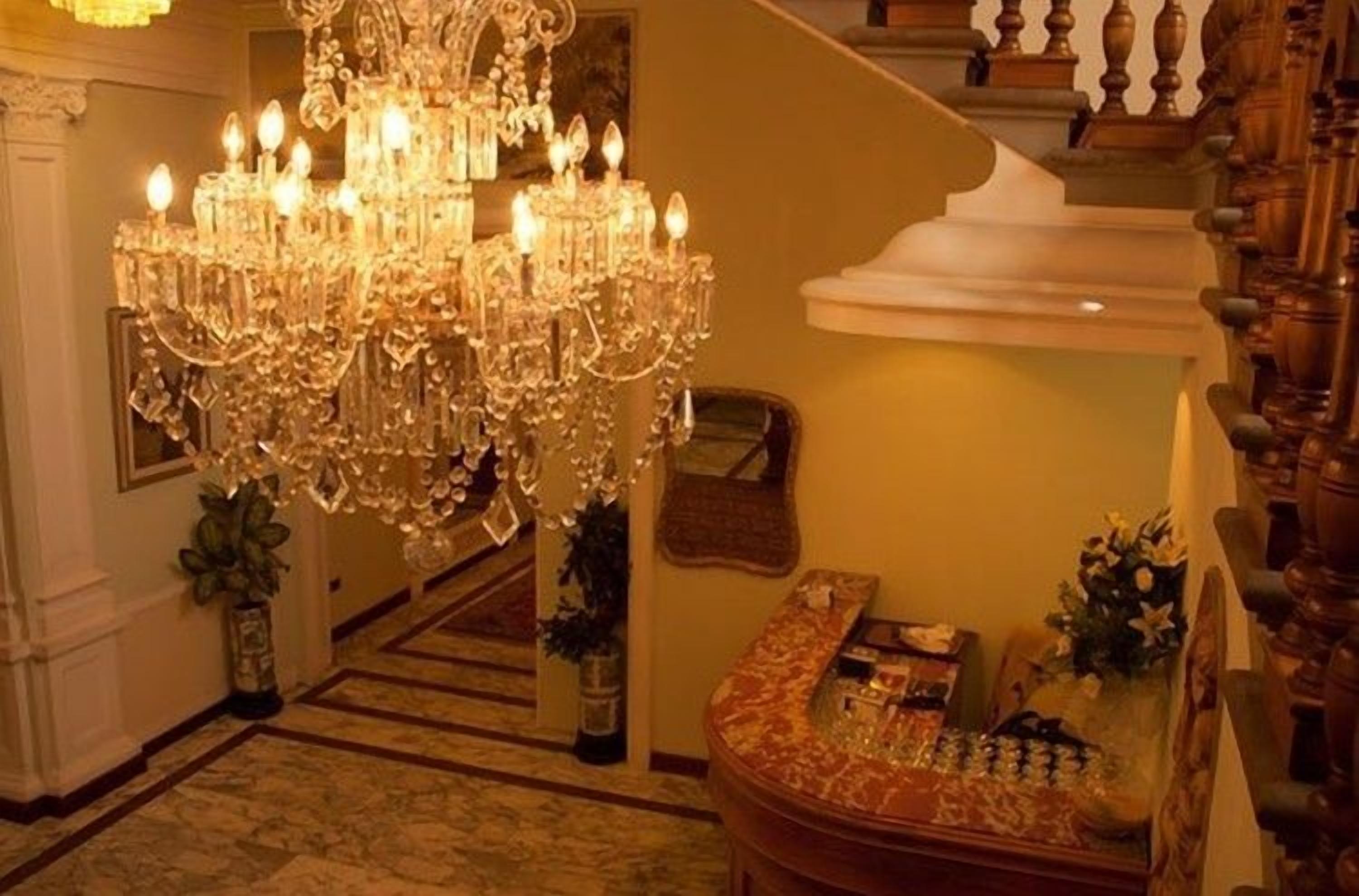 Un gran candelabro, una escalera y un área de recepción con un escritorio y sillas.