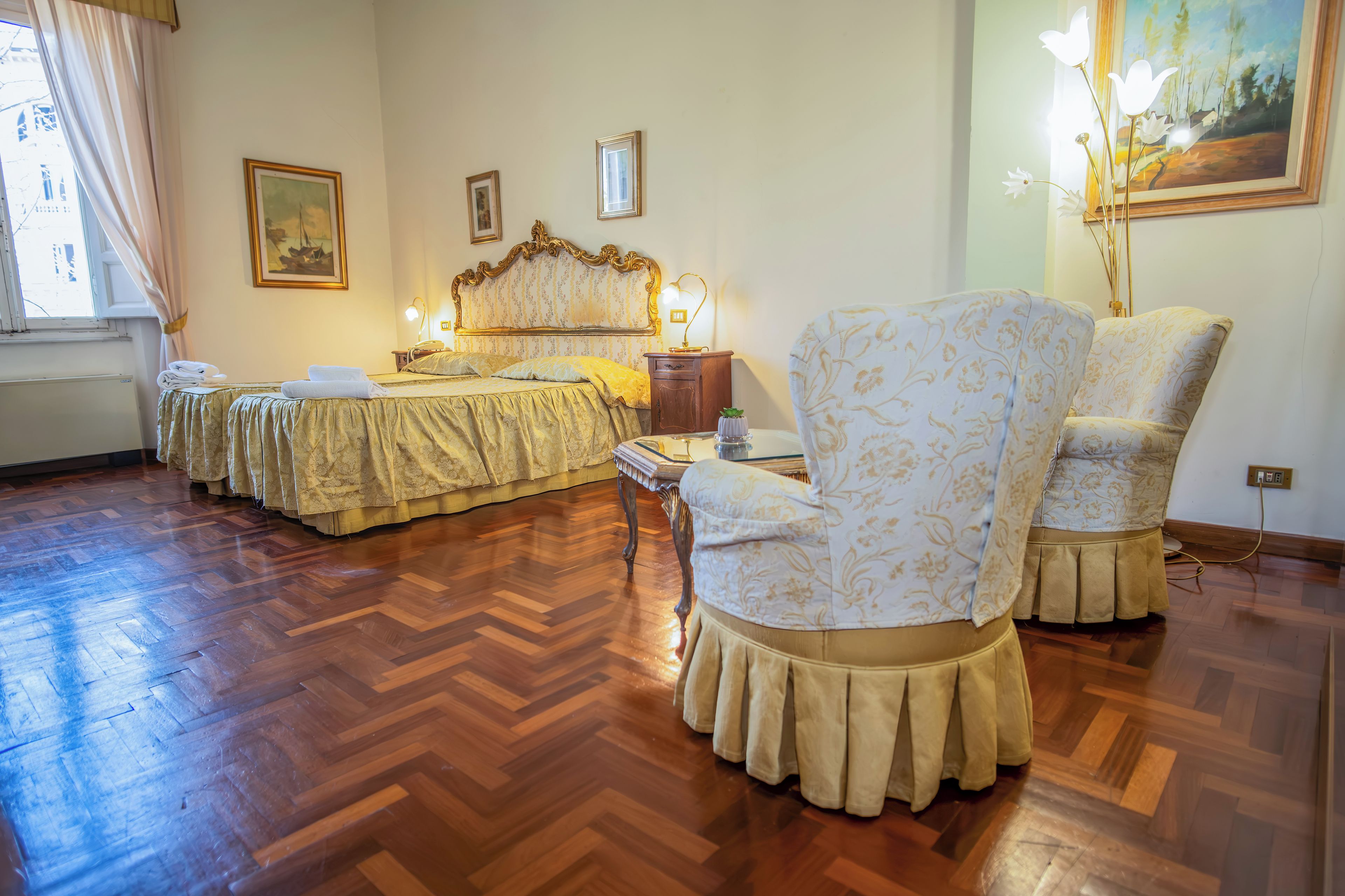 Ein Hotelzimmer mit einem großen Bett, zwei Sesseln, einem Nachttisch und einem Gemälde an der Wand.