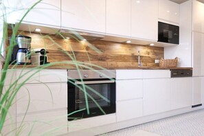 A modern kitchen with white cabinetry, a wooden countertop, a built-in oven, and a coffee maker. - Captain's House at the Friedrichs Lock (Carolinensiel-Harlesiel)