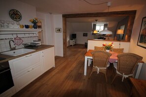 Eine Küche mit Spüle, Schränken und einem Essbereich mit Korbstühlen und einem Tisch.
