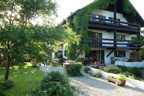 A two-story building with a sloped roof, surrounded by a well-maintained garden with various plants and a gravel path. - "s kleine Fischerhäusl" (Utting\/Ammersee)