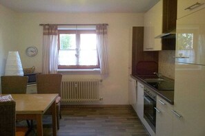 A compact kitchen with a dining table, chairs, a window with curtains, and a built-in oven. - 1 Country House Nina (Hohenschwangau)