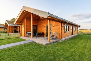 A modern log cabin with a covered patio, a dining area, and a small outdoor seating space. - Ferienhaus mit Eigener Sauna und Grossem Garten (Toenning)