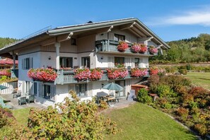 Ein mehrstöckiges Hotel mit Balkonen, die mit Blumen geschmückt sind, Sitzgelegenheiten im Freien und einem gepflegten Garten.