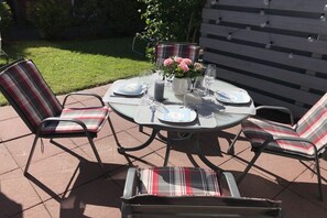 Une table de jardin ronde, idéale pour les repas en plein air, accompagnée de quatre chaises, chacune dotée d’un coussin à carreaux.