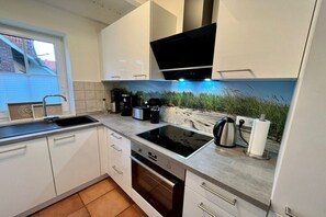 Une cuisine moderne avec des meubles blancs, une plaque de cuisson à induction noire et une grande fenêtre.