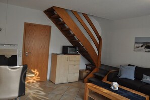 A compact living space with a wooden staircase, a kitchenette, a sofa, and a coffee table. - Holiday home Seemuschel (Cuxhaven Duhnen)