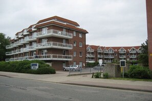A multi-story residential building with balconies, a paved driveway, and a street in front. - Residence Albatros (Apt. 16) (Cuxhaven-Döse)