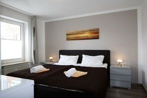 Ein Hotelzimmer mit einem Bett, zwei Nachttischen, einem Fenster und einem Gemälde an der Wand.