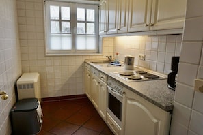 A kitchen with white cabinets, a stove, a sink, and a window. - Lindenhof Holiday Apartment No. 2 (Wenningstedt-Braderup)