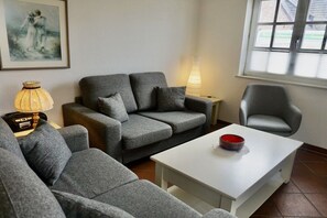 A living room with a grey sofa, a white coffee table, a lamp, and a chair. - Lindenhof Holiday Apartment No. 2 (Wenningstedt-Braderup)