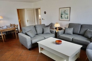 Ein Wohnzimmer mit grauen Sofas, einem weißen Couchtisch und einem Essbereich mit Tisch für vier Personen.