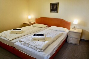 A double bed with two bedside tables, each with a lamp, in a room with plain walls and a single framed picture. - Lindenhof Holiday Apartment No. 2 (Wenningstedt-Braderup)
