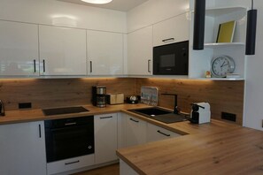A modern kitchen with white cabinetry, a built-in oven, a microwave, and a coffee maker. - House Carola Apartment 15 (Wenningstedt-Braderup)