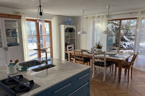 A kitchen with a large island, wooden dining table, and chairs, with a view of a snowy landscape through the windows. - Holiday home with 4 bedrooms (Wessobrunn)