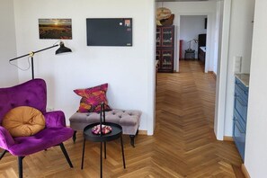 Ein modernes Wohnzimmer mit einem violetten Sessel, einem grauen Sofa und einem Holzboden mit Fischgrätmuster.