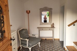 Ein Zimmer mit einem Sessel, einem kleinen Tisch, einem Spiegel und einem gemusterten Boden.
