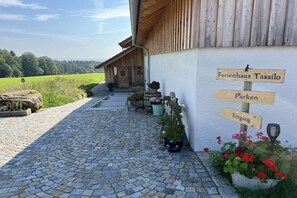 A rustic building with a cobblestone path leading to a wooden door, surrounded by potted plants and a signpost indicating directions to 'Ferienhaus Tassilo', 'Parken', and 'Eingang'. - Holiday home with 4 bedrooms (Wessobrunn)