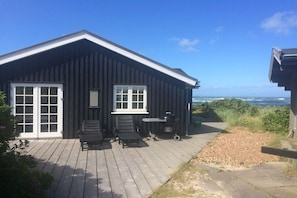 Eine Holzhütte mit einer Terrasse, zwei Stühlen, einem Tisch und einem Grill.
