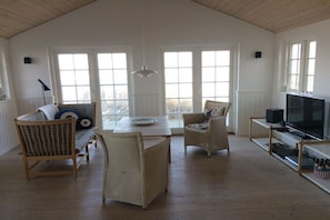 Ein geräumiges Zimmer mit hoher Decke, großen Fenstern, einem Fernseher und Korbmöbeln.