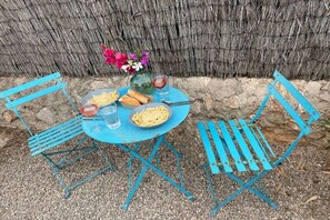 A round table with a blue metal frame, accompanied by two blue metal chairs. The table is set with a plate of food, a glass of red liquid, and a vase with flowers. - Holiday home with 2 bedrooms (Cala Llombards)