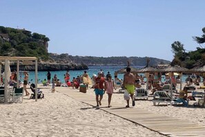 A beach with a wooden walkway, umbrellas, and beach chairs. - Holiday home with 2 bedrooms (Cala Llombards)