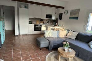 A modern kitchen with white cabinets, a microwave, and a stove. There is a gray sofa with patterned cushions and a small wooden table with a vase of flowers. - Holiday home with 2 bedrooms (Cala Llombards)