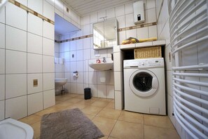 A compact laundry room with a washing machine, a sink, and a toilet. - Apartment 'Festungsblick' with Terrace, Garage and Private Entrance (Koblenz)