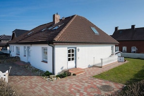 Ein eingeschossiges Haus mit Ziegeldach, weißer Fassade und kleinem Vorgarten mit gepflastertem Zugang.