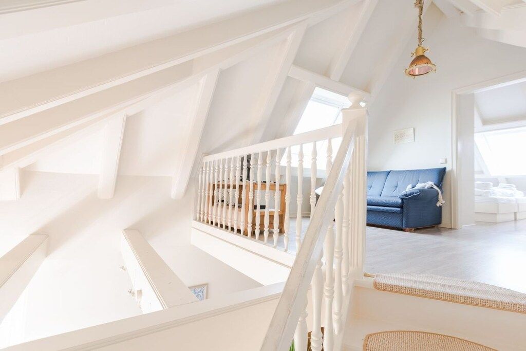 Une pièce aux hauts plafonds, avec un escalier blanc, un canapé bleu et un luminaire suspendu.