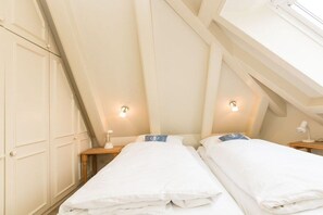 Ein Zimmer mit zwei Betten, einer geneigten Decke und einem Fenster.