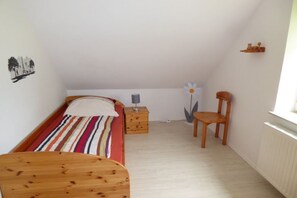 Quarto pequeno e acolhedor com uma cama de solteiro, mesa de cabeceira, cadeira e radiador.