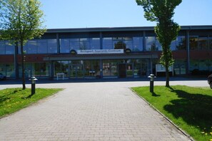Un bâtiment sur lequel on peut lire l’inscription « Reitsport-Touristik-Centrum », avec une entrée pavée et deux arbres de chaque côté.