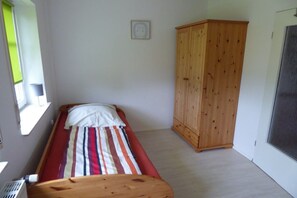 Ein kleines Zimmer mit einem Einzelbett, einem Holzschrank und einem Fenster.
