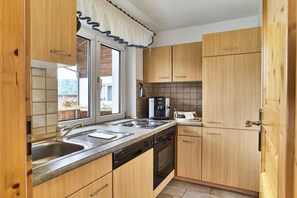 A compact kitchen with wooden cabinets, a built-in oven, and a window with a curtain. - 3 Country House Farmer (Bodenmais)