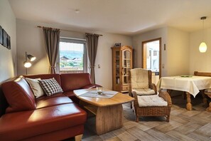 A cozy living room with a leather sofa, a wooden coffee table, a wicker armchair, and a dining table with a white tablecloth. - 3 Country House Farmer (Bodenmais)