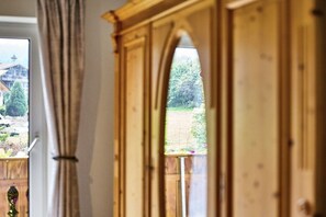 A wooden wardrobe with a mirrored door, a window with curtains, and a view of a garden and a building outside. - 3 Country House Farmer (Bodenmais)