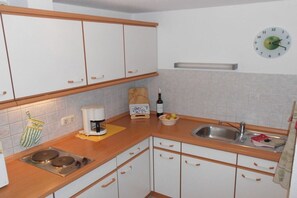 Eine Küche mit weißen Schränken, einem Spülbecken, einer Kaffeemaschine und einer Uhr an der Wand.