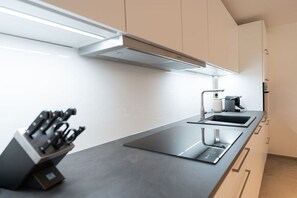 A modern kitchen with a sleek countertop, a built-in knife block, a sink, and a stove. - Holiday apartment Villa Alpjuwel-Mondblick (Oberstdorf)