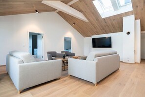 Un salon moderne avec deux canapés, une table à manger et un téléviseur à écran plat fixé au mur.