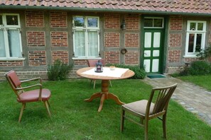 Ein Ziegelhaus mit einer grünen Tür, ein runder Holztisch mit Stühlen und eine Laterne auf dem Tisch.