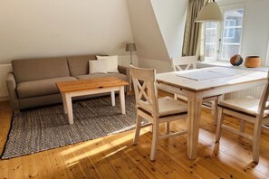A cozy living room with a sofa, a wooden coffee table, and a dining table with chairs. - Holiday apartment with 2 bedrooms (Norddorf)