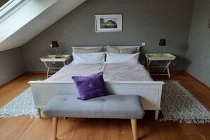 A bedroom with a sloped ceiling, a bed with white bedding, two bedside tables with lamps, a bench, and a patterned rug. - Holiday home in Holsthum with Wi-Fi (Holsthum)