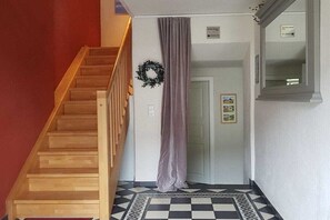 Eine Treppe mit hölzernen Stufen führt zu einer Zwischenebene, mit einem grauen Vorhang und einem schwarz-weißen Bodenbelag.