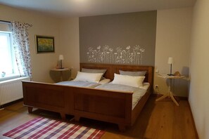 Un dormitori amb un llit de fusta, una finestra amb cortines, una obra d'art penjada a la paret i una petita taula de nit.