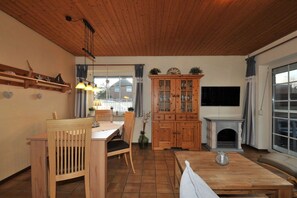 Un salon chaleureux avec un plafond en bois, une table à manger avec des chaises, un buffet aux portes vitrées et une cheminée.