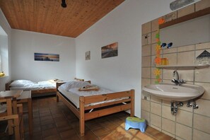 Ein Zimmer mit zwei Holzbetten, einem Waschbecken und einem kleinen Hocker.