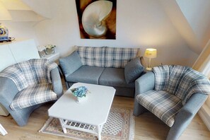 Ein gemütliches Wohnzimmer mit einer Couch, zwei Sesseln, einem Couchtisch und einer Lampe.