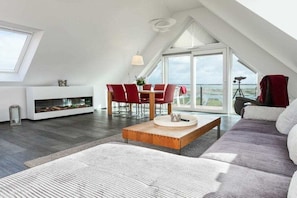 A modern loft bedroom with a sloped ceiling, a large window, a fireplace, and a dining area with red chairs. - Apartment in Juist with Wi-Fi and water park (Juist)