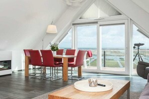 A modern dining area with a table and chairs, a large window with a view, and a telescope on a tripod. - Apartment in Juist with Wi-Fi and water park (Juist)